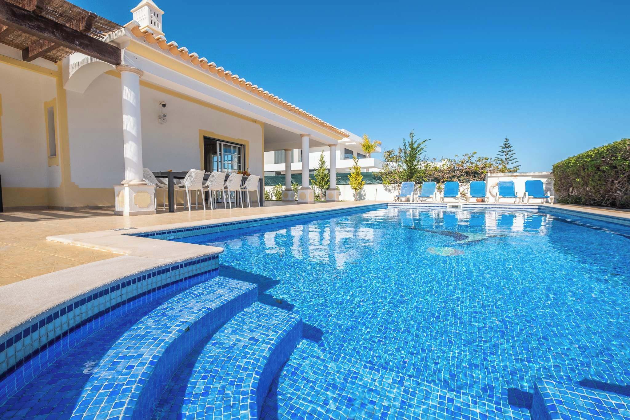 A swimming pool with tiled steps, white columns, and blue lounge chairs.