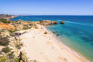 A coastal beach with rocky cliffs, a sandy beach, and clear blue waters.