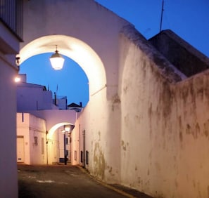 A narrow alleyway with a white building on the left and a large archway overhead. - Apartment Aiko - Downtown Albufeira (Albufeira)