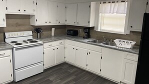 A compact kitchen with white cabinets, a stove, a microwave, and a sink. - Cozy Gilbert House (Gilbert)