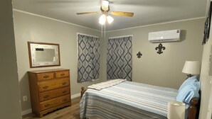A bedroom with a bed, a wooden dresser, a ceiling fan, patterned curtains, and an air conditioning unit. - Cozy Gilbert House (Gilbert)