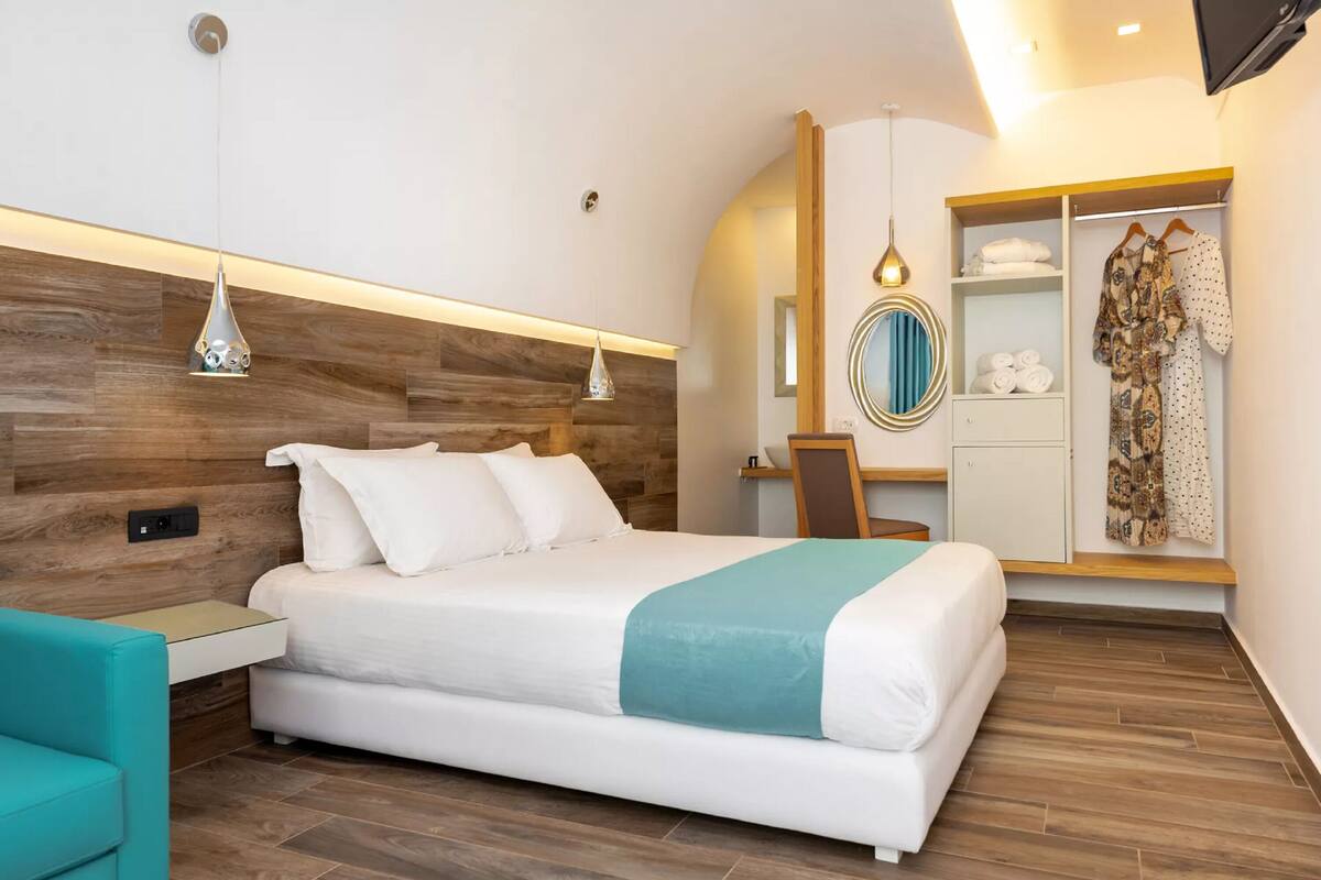 A modern hotel room with a large bed, a desk, a wardrobe, and a mirror.