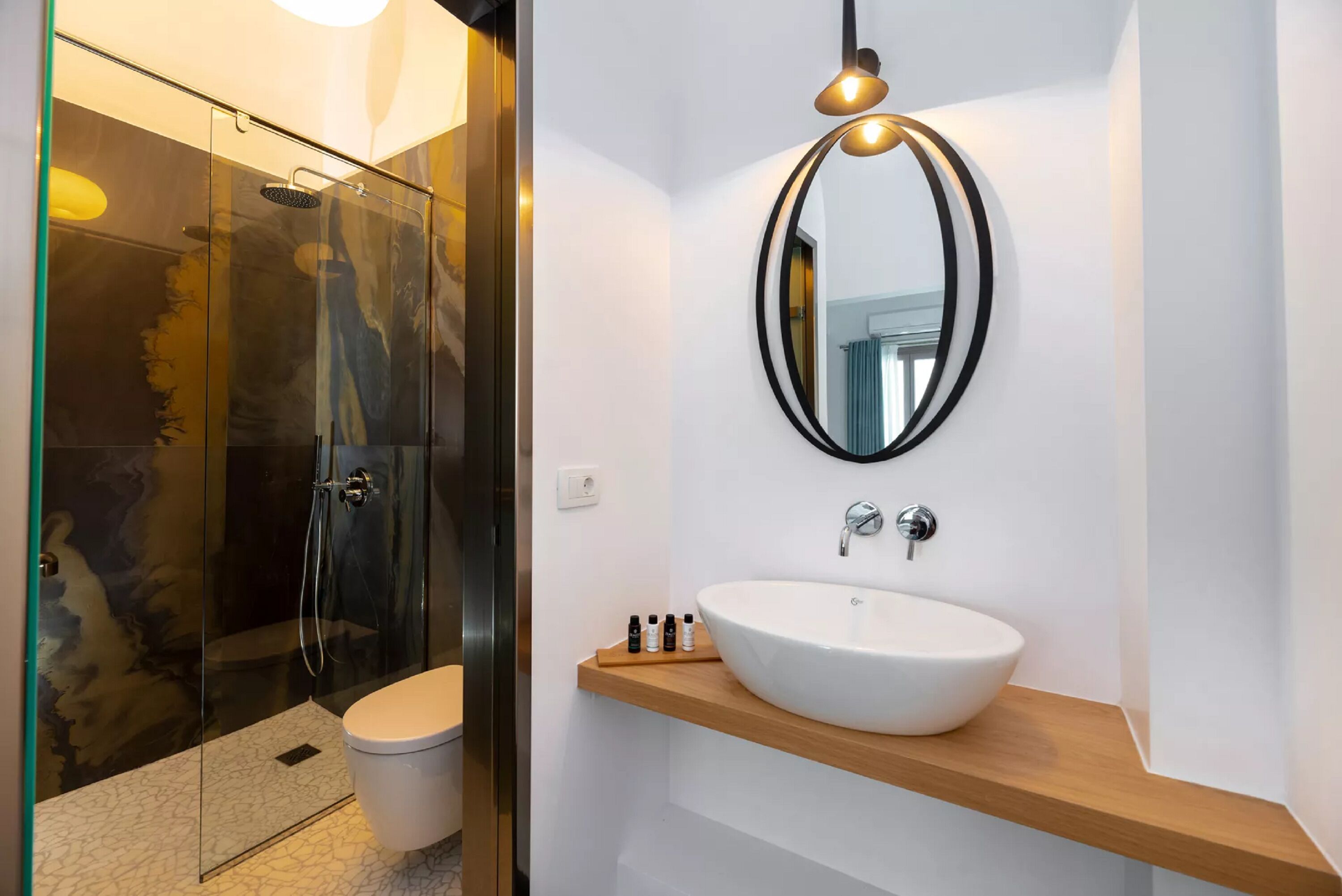 A modern bathroom with a glass-enclosed shower, a white sink with a wooden countertop, and a round mirror with a black frame.