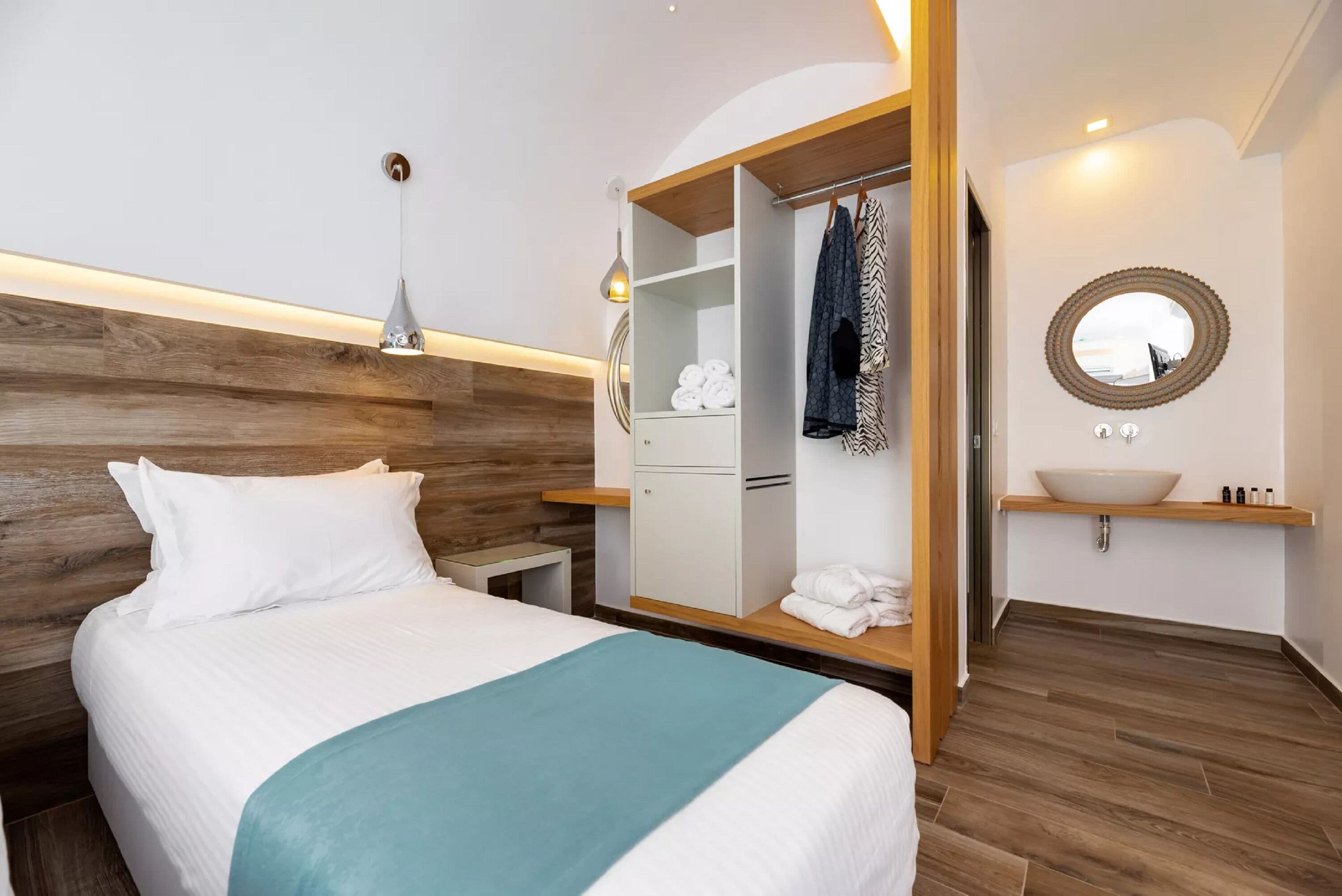 Una habitación de hotel ordenada con una cama, un armario, un tocador con espejo y una mesita de noche.