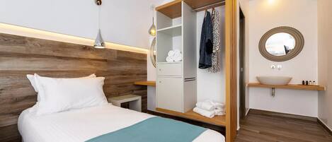 Una habitación de hotel ordenada con una cama, un armario, un tocador con espejo y una mesita de noche.
