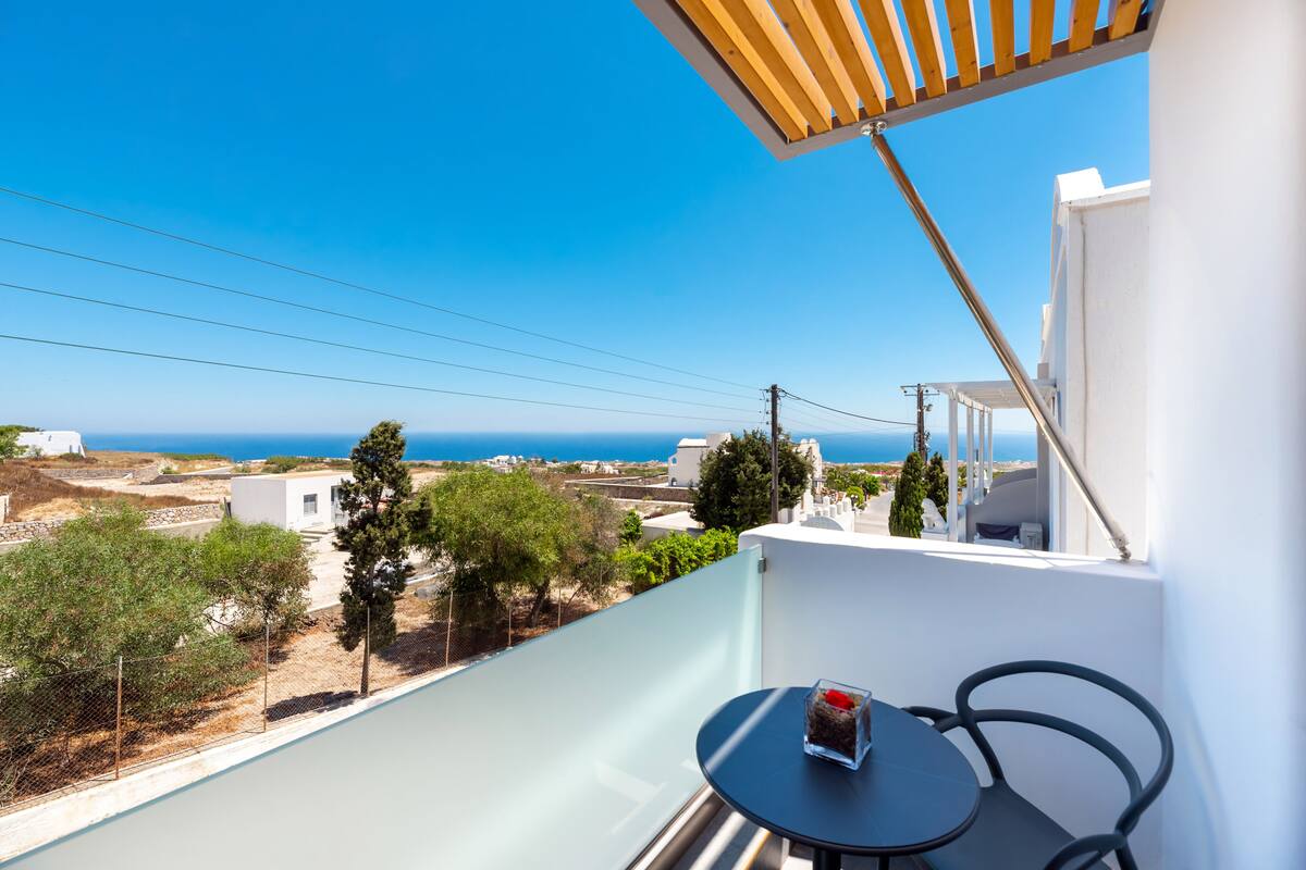 A balcony with a view of the sea, a table with a glass container, and a wooden pergola.