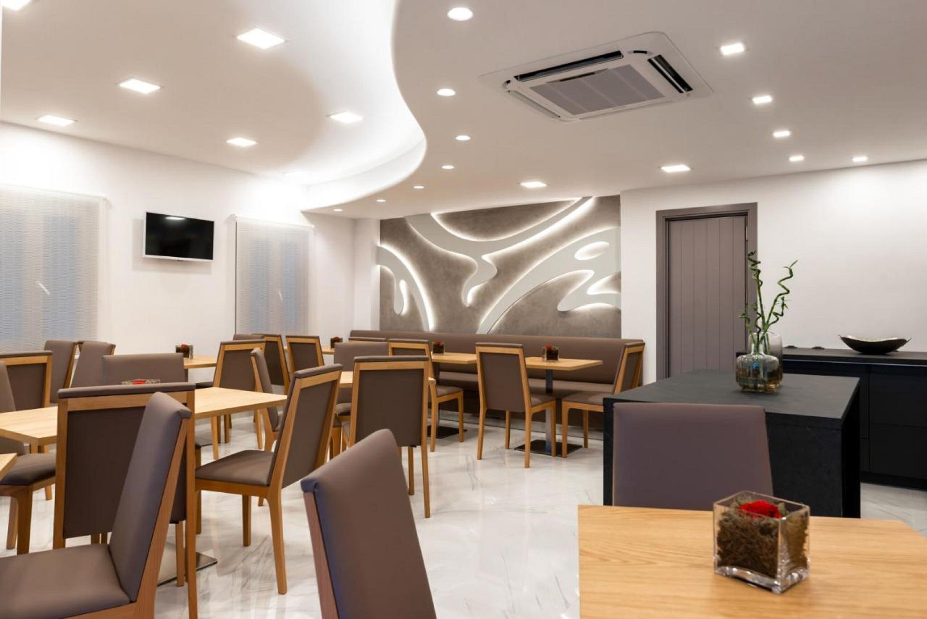 Un espace de restauration moderne avec des tables et des chaises en bois, un éclairage encastré au plafond et un mur décoratif.