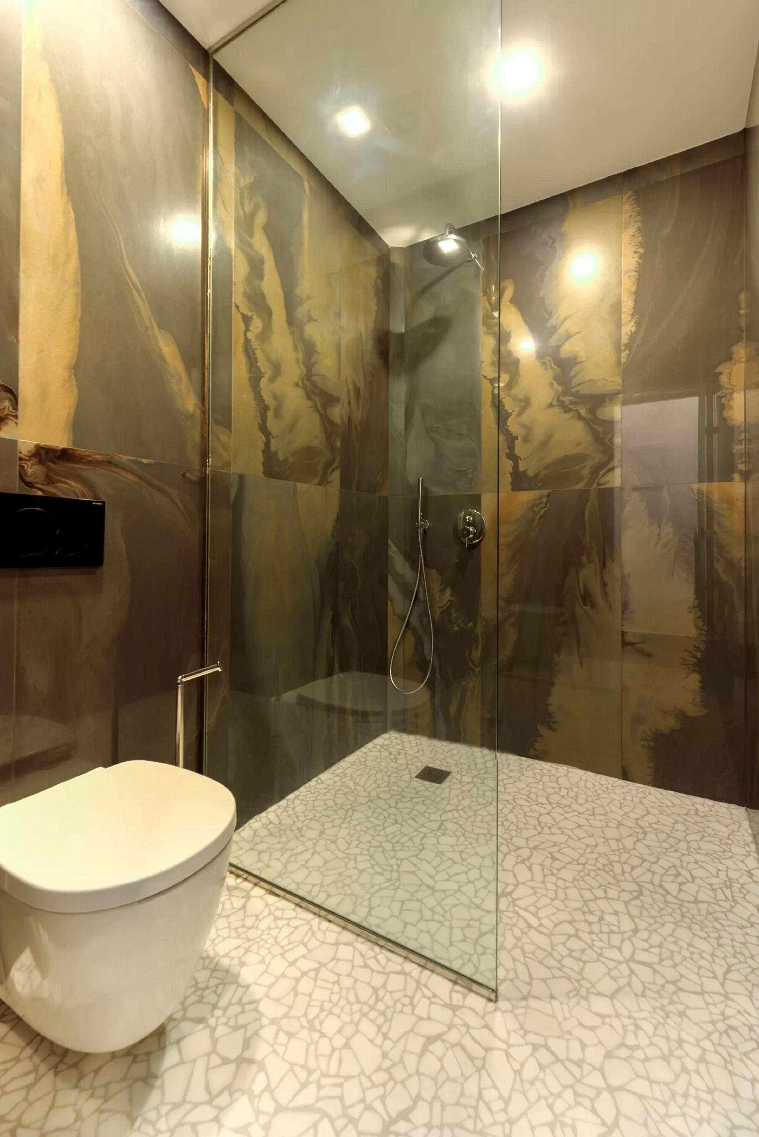 Ein modernes Badezimmer mit einer gläsernen Duschkabine, einer weißen Toilette und einem Boden mit Marmoroptik.