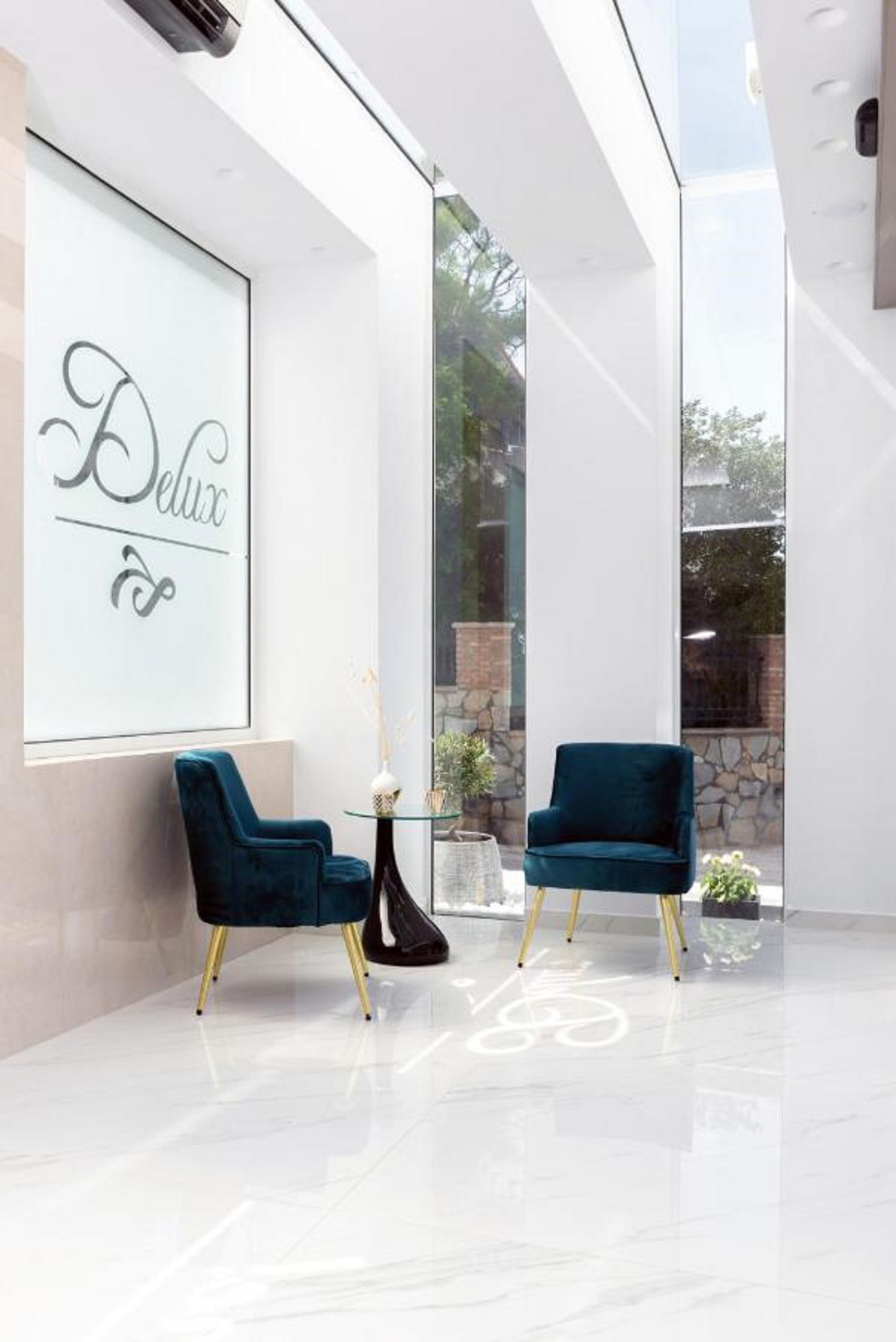 A modern interior with two dark blue velvet chairs, a glass table, and a framed sign on the wall.