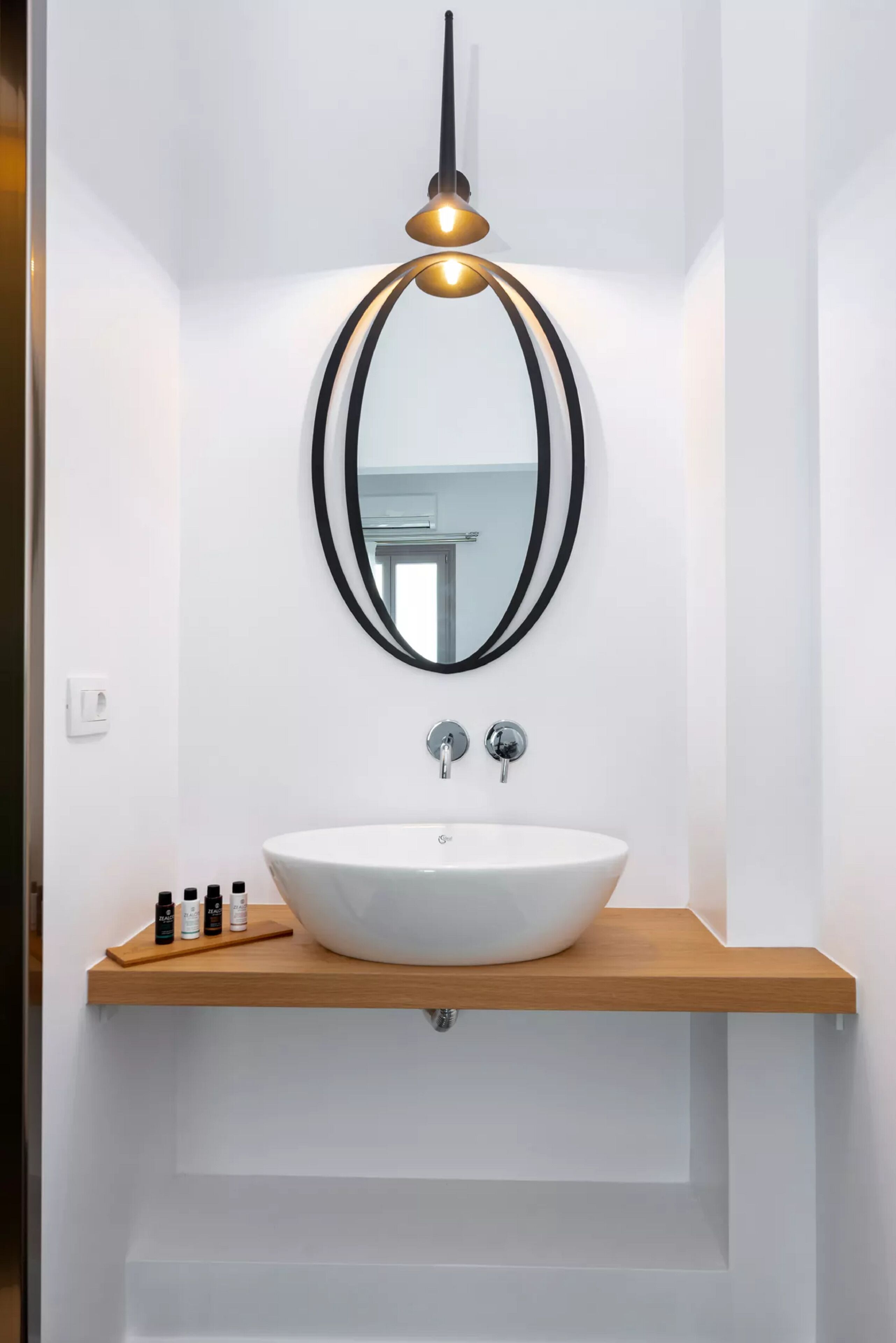 Ein Badezimmer mit einem weißen Waschbecken, einem Spiegel mit schwarzem Rahmen und einer Pendelleuchte.