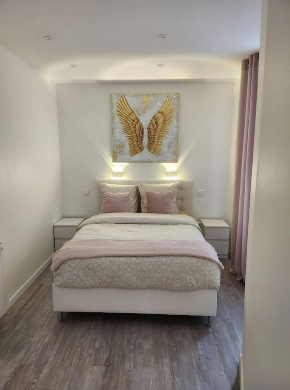 A bedroom with a large bed, two bedside tables, a wall-mounted light, and a ceiling light.