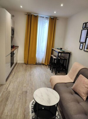 A compact living space with a sofa, a small round table, a kitchen area, and a dining table with chairs.