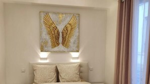 Un dormitorio con una cama grande, dos mesitas de noche, una lámpara de pared y un cuadro decorativo con forma de ala dorada.