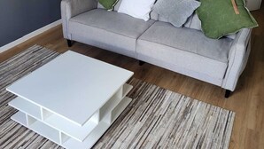 A living room with a grey sofa, white coffee table, and a wooden dining table. - Modern, fully-equipped apartment (L'Isle-Jourdain)