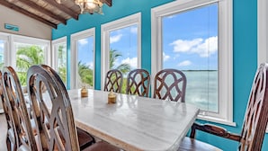 A dining area with a marble table and wooden chairs, large windows with a view of the ocean, and a ceiling with exposed beams and pendant lights. - Beachfront 3B/3B Fishing Oasis (Ramrod Key)