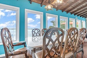 A dining area with a view of the ocean, featuring wooden chairs and a white table. - Beachfront 3B/3B Fishing Oasis (Ramrod Key)