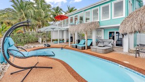 A swimming pool with lounge chairs and umbrellas, surrounded by a house with a balcony and palm trees. - Beachfront 3B/3B Fishing Oasis (Ramrod Key)