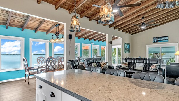 A spacious kitchen with a large island, wooden ceiling beams, and large windows offering a view of the outdoors. - Beachfront 3B/3B Fishing Oasis (Ramrod Key)