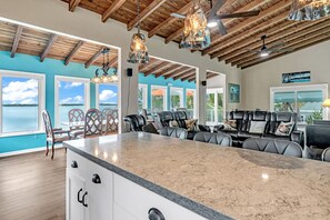 A spacious kitchen with a large island, wooden ceiling beams, and large windows offering a view of the outdoors. - Beachfront 3B/3B Fishing Oasis (Ramrod Key)