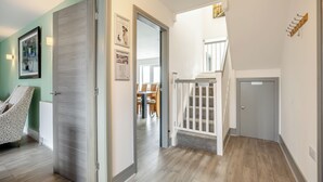 Un couloir avec une porte donnant sur une pièce meublée de façon originale, un escalier et une vue sur un coin repas.