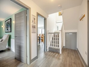 Um corredor com uma porta que dá para um quarto com mobiliário estampado, uma escadaria e vista para uma sala de jantar.