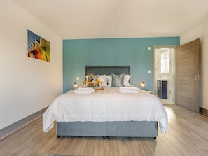 A bedroom with a bed, bedside tables, a painting, and a door.