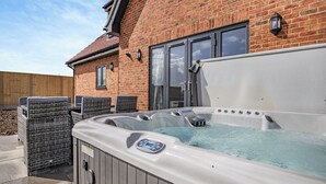 Un bain à remous doté d’un panneau de commande, deux fauteuils en osier et une maison en briques avec une fenêtre et une porte.