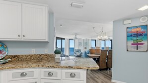A modern kitchen with white cabinets, granite countertops, and a dining area with a view of the ocean. - Great Rates! Book Now and Save*2BR/2BA On Beach*Sleeps 8*7th floor (Orange Beach)