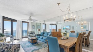 A spacious living room with a large window, a dining area with a wooden table and wicker chairs, and a blue sofa. - Great Rates! Book Now and Save*2BR/2BA On Beach*Sleeps 8*7th floor (Orange Beach)
