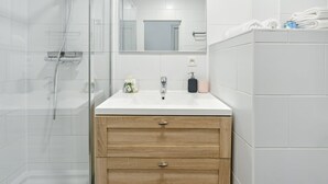 Une salle de bain moderne avec une douche à parois de verre, un lavabo blanc avec un meuble-vasque en bois, et des serviettes soigneusement pliées sur une étagère.