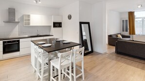 Une cuisine moderne avec des meubles blancs, un îlot central doté de chaises, une table à manger et un canapé dans l’espace salon.