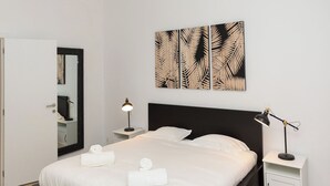 Une chambre moderne avec un grand lit, deux tables de chevet, une commode, un miroir mural et une œuvre d’art décorative accrochée au mur.