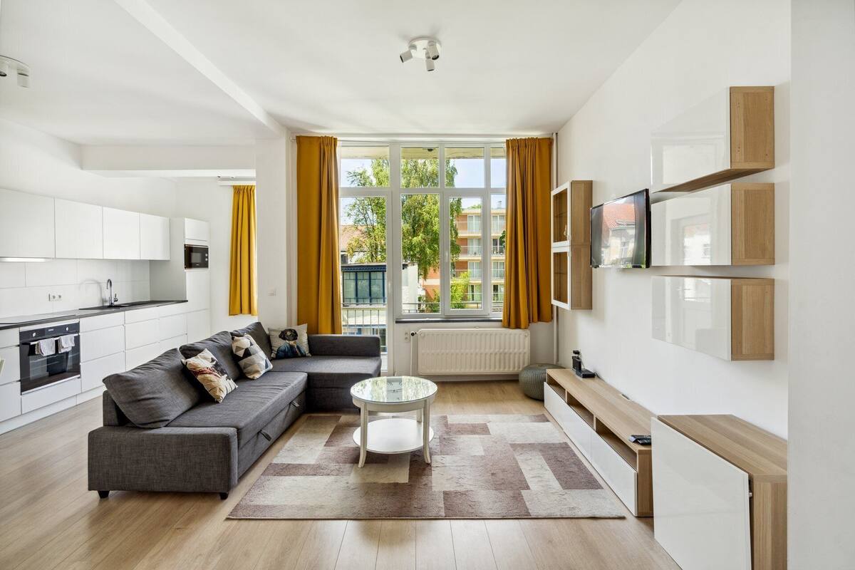 Un apartamento moderno con cocina, sala de estar y un amplio ventanal con cortinas.
