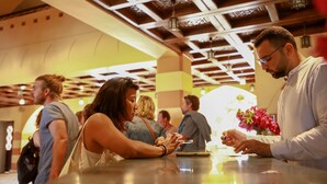 Un groupe de personnes se trouve au comptoir d’accueil d’un bâtiment doté d’un plafond haut et d’un éclairage décoratif.