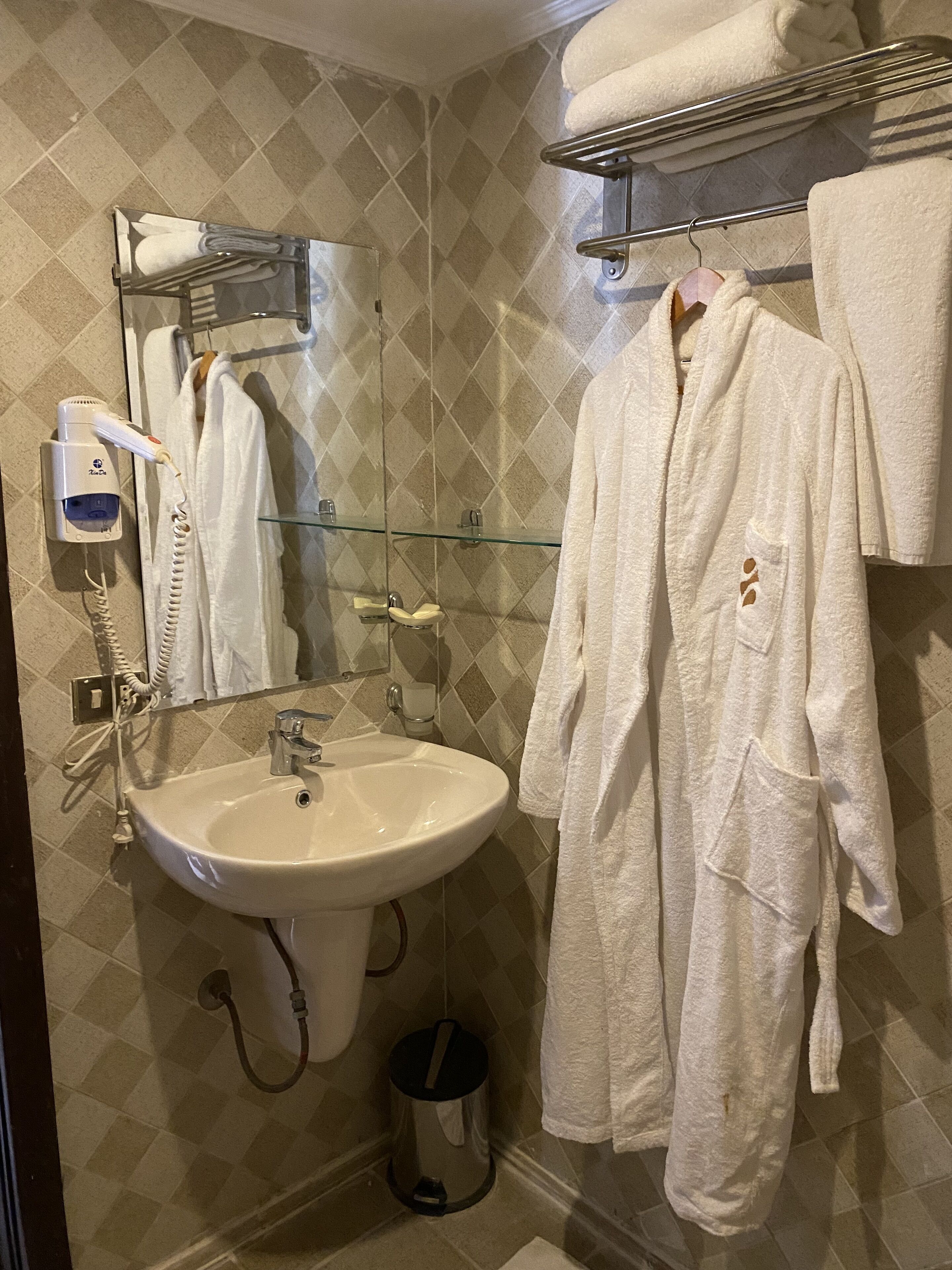 Een badkamer met een wastafel, spiegel, handdoekhouder en een haardroger.