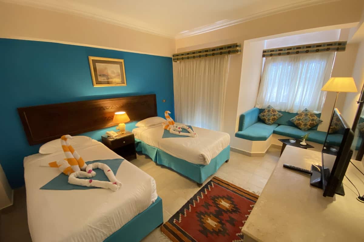 A hotel room with two beds, a sofa, a TV, and a lamp.