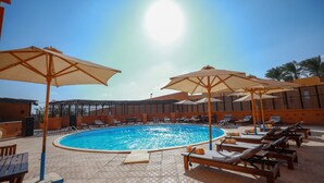 Un espace piscine doté de chaises longues et de parasols, entouré d’une terrasse carrelée.