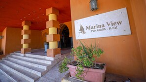 L’entrée d’un hôtel, avec une enseigne indiquant « Marina View Port Ghalib – Hôtel », un escalier et un bac à fleurs contenant des plantes.