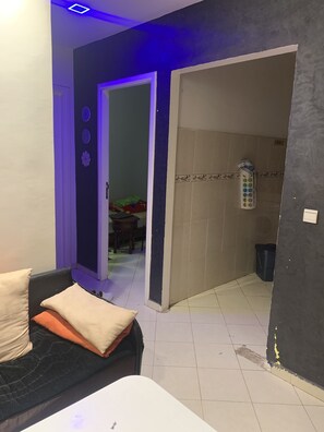 Une pièce avec un canapé noir, une table blanche et une porte qui donne sur une autre pièce.