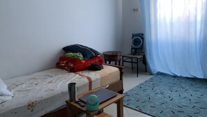 Une petite pièce propre et bien rangée, avec un lit, un bureau et une chaise. On y trouve une petite table sur laquelle sont posés un ordinateur portable et une tasse.