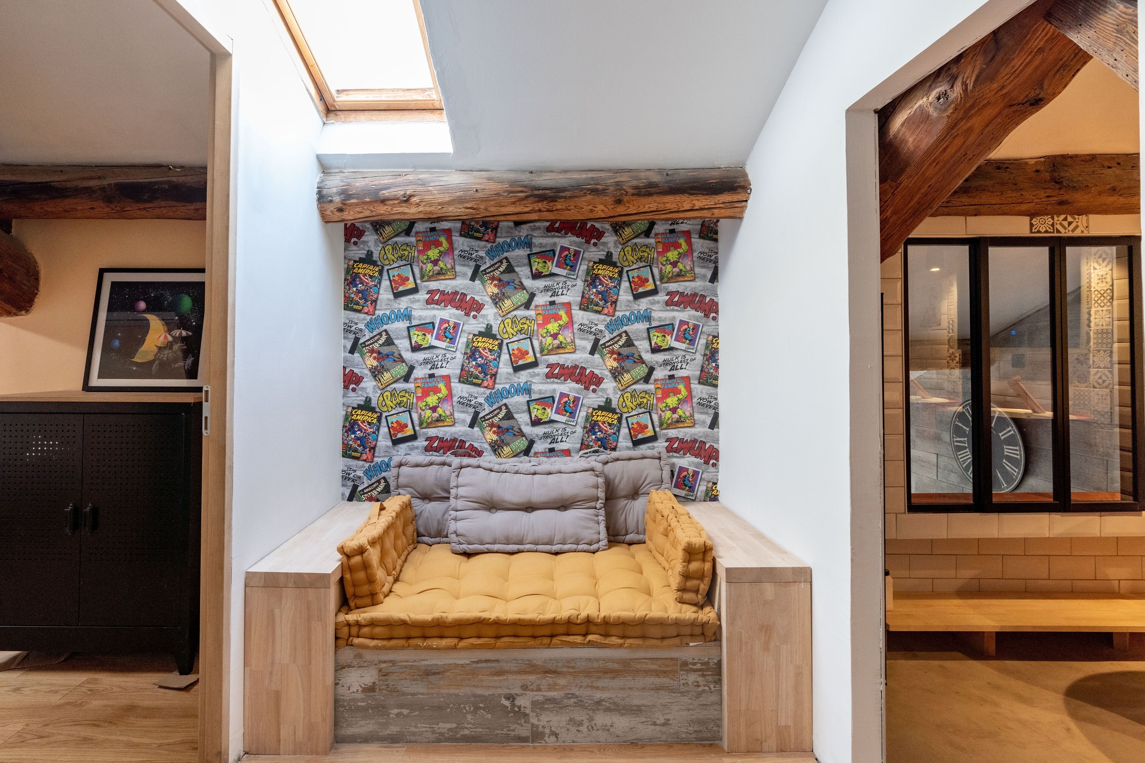 A cozy alcove with a cushioned bench, a wall adorned with comic book posters, and a wooden ceiling beam.