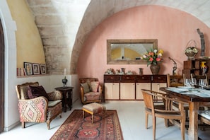Um quarto aconchegante com uma mesa de jantar de madeira, cadeiras, um tapete estampado, um sofá e um armário com objetos decorativos.
