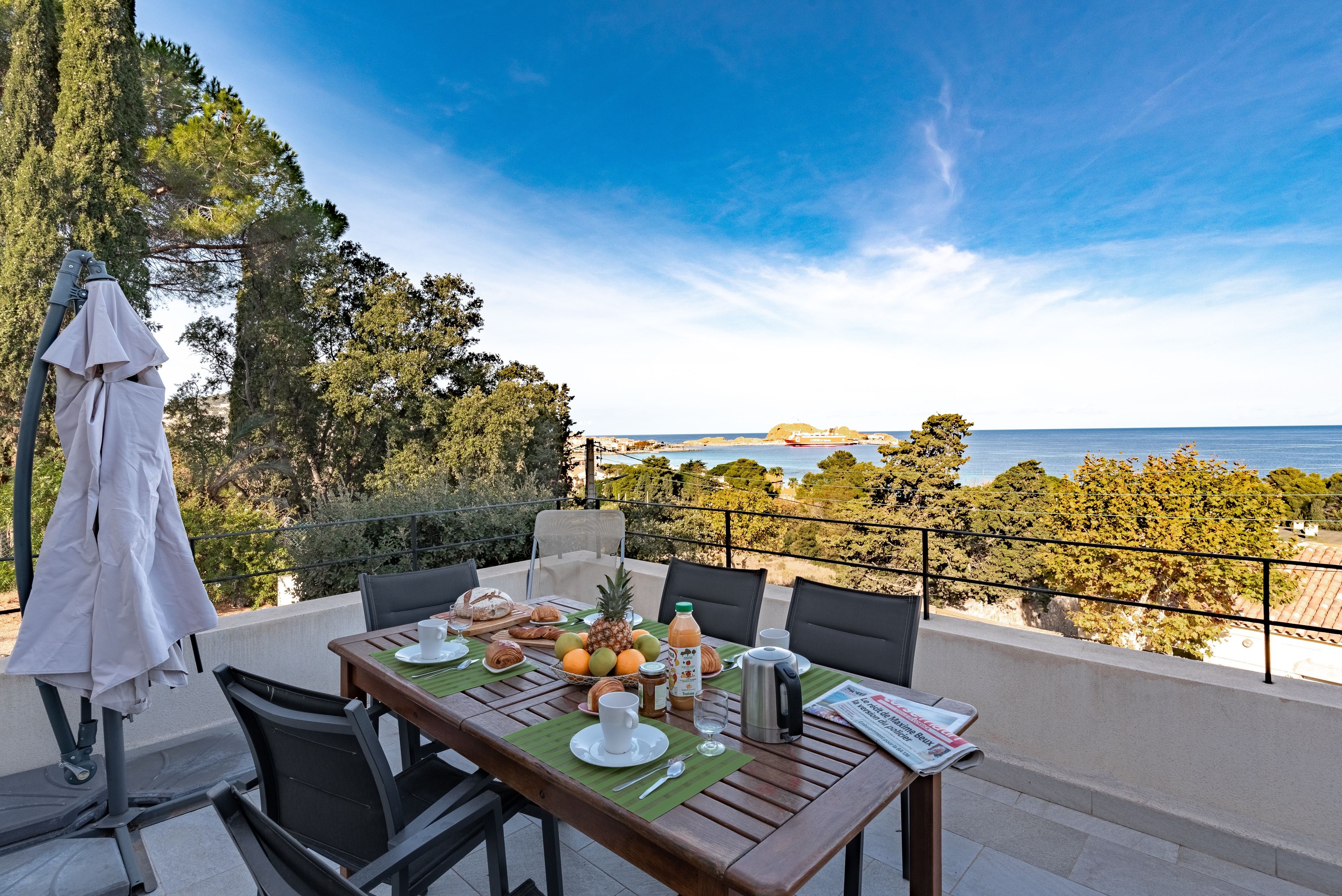 An outdoor dining area with a table set for two, overlooking a coastal view.