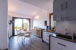 A modern kitchen with a dining area, large windows, and a view of the outdoors.