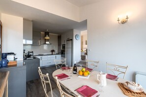 Une cuisine moderne avec un coin repas, comprenant un îlot central, des meubles blancs et une horloge murale.