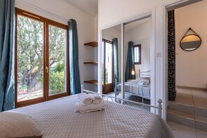 A bedroom with a large window, a bed with neatly folded towels, a wardrobe, and a mirror.