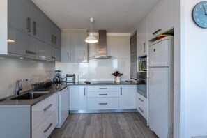 Une cuisine moderne avec des meubles gris, un four encastré et un réfrigérateur en acier inoxydable.