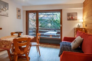 Habitació acollidora amb taula de dinar, cadires, un sofà i vista a un jardí a través d'una porta corredissa.