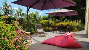 Eine Terrasse im Freien mit zwei Holzliegen, einem rosa Sitzsack und zwei großen Sonnenschirmen.