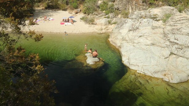 Ein Naturbad, umgeben von felsigem Gelände, mit Menschen, die schwimmen und am Ufer entspannen.